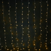 Solar powered warm white 160 LED curtain light hanging outdoors, glowing in a cascading pattern