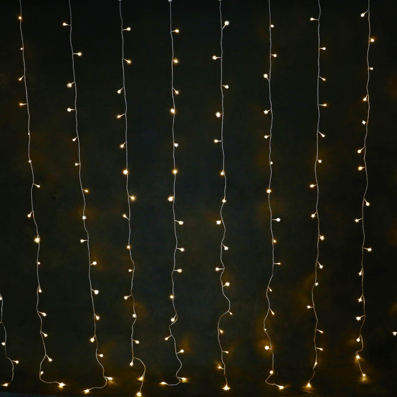 Solar powered warm white 160 LED curtain light hanging outdoors, glowing in a cascading pattern
