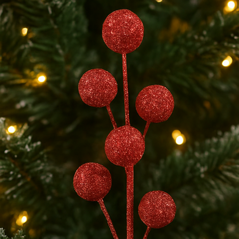 Red glittery berry branch decoration on a Christmas tree with blurred lights in the background