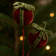 Red ornaments with green ribbons on a Christmas tree with blurred lights in the background