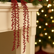 Red berry garland on a fireplace mantle with a blurred Christmas tree in the background.