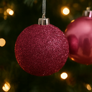 Purple glittery Christmas ornament on a tree with blurred lights in the background