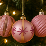 Pink and gold Christmas ornaments with snowflake design on a tree.
