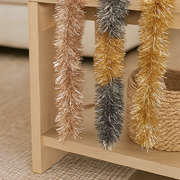 Decorative tinsel garlands in gold and silver on a wooden shelf.