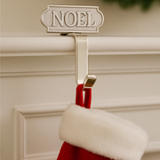 Red stocking with white fur trim hanging from a 'NOEL' sign on a beige wall.