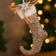 Gold glittery Christmas stocking with a snowflake ornament against a blurred festive background.