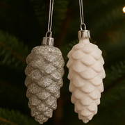 Two glittery pine cone ornaments hanging against a green foliage background