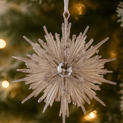 Decorative snowflake ornament with a gemstone center against a Christmas tree background