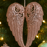 Decorative angel wings ornament on a Christmas tree with lights in the background