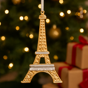 Gold Eiffel Tower ornament hanging in front of a Christmas tree with lights and presents.
