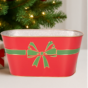 Red metal planter with green bow design in front of a Christmas tree