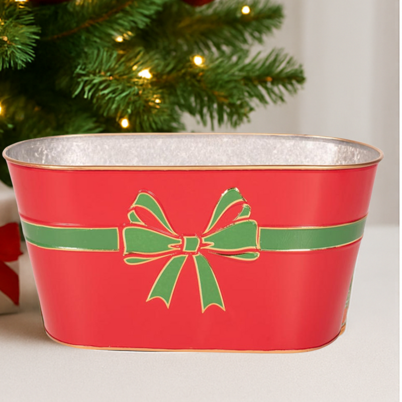 Red metal planter with green bow design in front of a Christmas tree