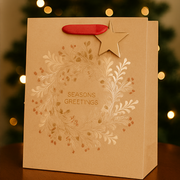 Brown gift bag with 'Seasons Greetings' text and star design against a blurred Christmas tree background.