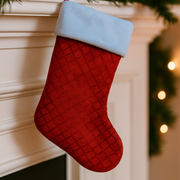 Red Christmas stocking with a blue cuff hanging on a fireplace.