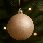 Gold glittery Christmas ornament hanging on a tree with blurred lights in the background