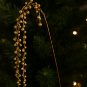 Decorative gold beads on a branch against a dark background with blurred lights