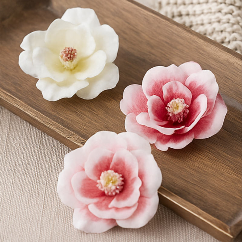 Three floral hair clips in white, pink, and red on a wooden surface.
