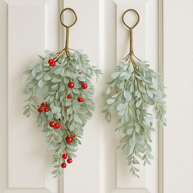 Two green leafy wreaths with red berries hanging on a white door.