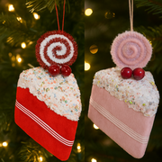 Two Christmas tree ornaments shaped like cake slices with decorative swirls and berries, set against a blurred Christmas tree background.