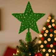 Green star-shaped Christmas tree topper on a decorated tree with blurred lights in the background.