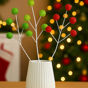 Decorative branches with green and red balls in a white vase against a festive background with lights.