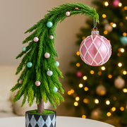 Decorative Christmas tree with pink and green ornaments against a blurred festive background.