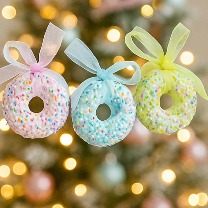 Three colorful donut ornaments with ribbons on a blurred Christmas tree background.