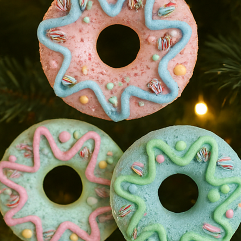 Three colorful donuts with decorative icing on a blurred Christmas tree background.