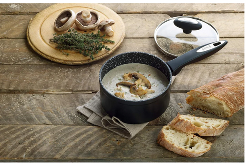 Black saucepan with mushroom soup on a wooden table with bread and herbs.