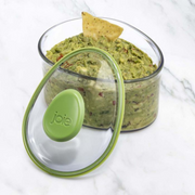 Glass container with guacamole and a tortilla chip, featuring a green lid with 'joie' branding. – thumbnail