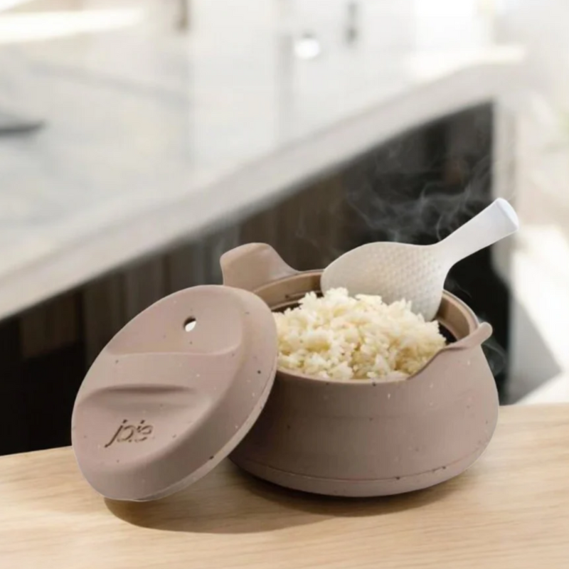Ceramic color rice cooker with steaming rice and a spoon on a kitchen counter.